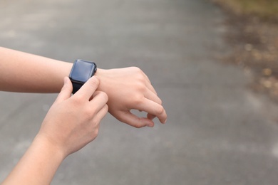 Photo of Young woman checking pulse with smartwatch on street, closeup. Space for text
