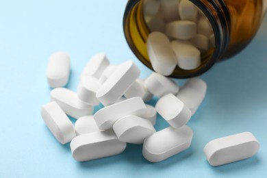 Photo of Bottle and vitamin capsules on light blue background, closeup