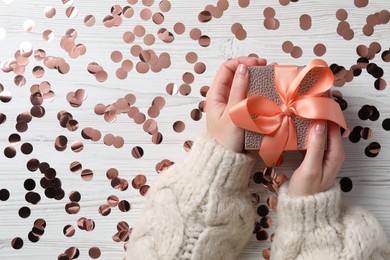 Photo of Christmas present. Woman with gift box and confetti on white wooden background, top view. Space for text