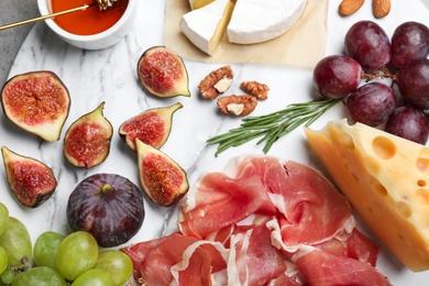 Photo of Delicious ripe figs, prosciutto and cheeses served on white board, flat lay
