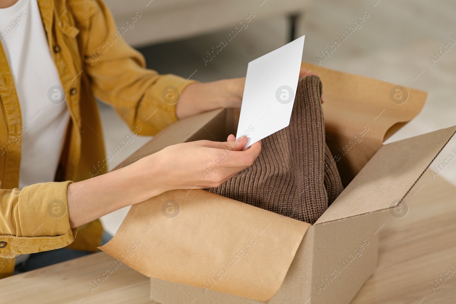 Photo of Woman holding greeting card near parcel with Christmas gift indoors, closeup