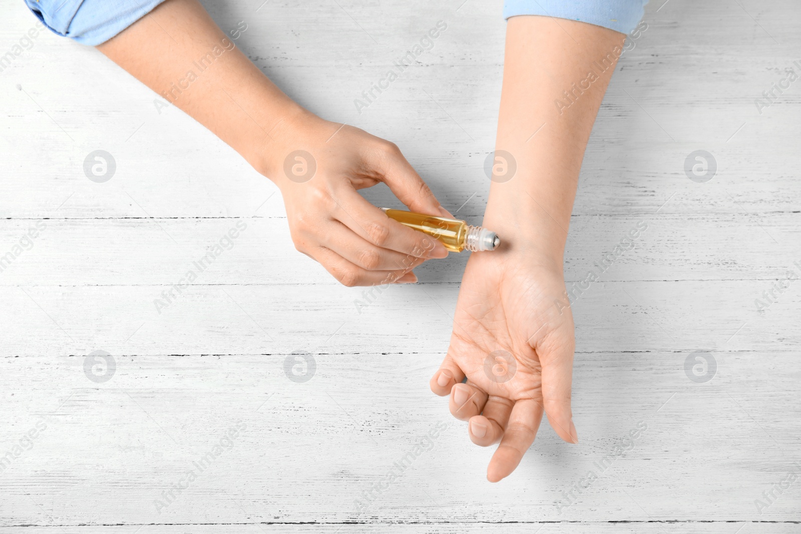 Photo of Woman applying essential oil on her wrist against white wooden background, top view. Space for text