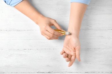 Woman applying essential oil on her wrist against white wooden background, top view. Space for text