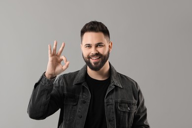 Portrait of bearded young man showing OK gesture on grey background