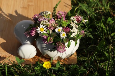 Photo of Ceramic mortar with pestle, different wildflowers and herbs on green grass outdoors