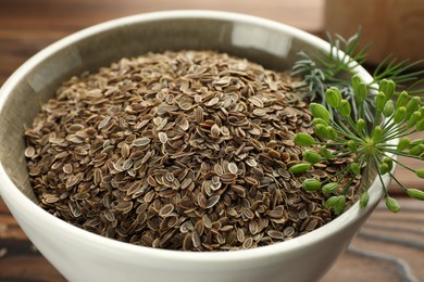 Photo of Bowl of dry seeds and fresh dill on table, closeup