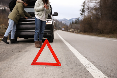 Photo of Man and woman near broken car outdoors, focus on emergency stop sign. Winter day