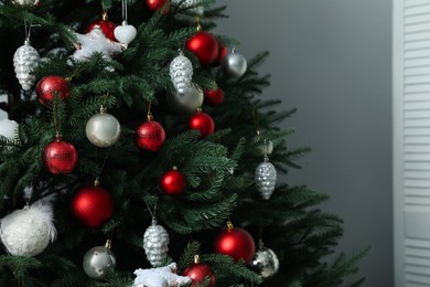 Photo of Beautifully decorated Christmas tree near grey wall indoors, closeup