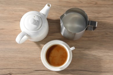 Photo of Aromatic tea with milk in cup, teapot and pitcher on wooden table, flat lay