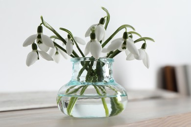 Photo of Beautiful snowdrop flowers in glass vase on wooden table