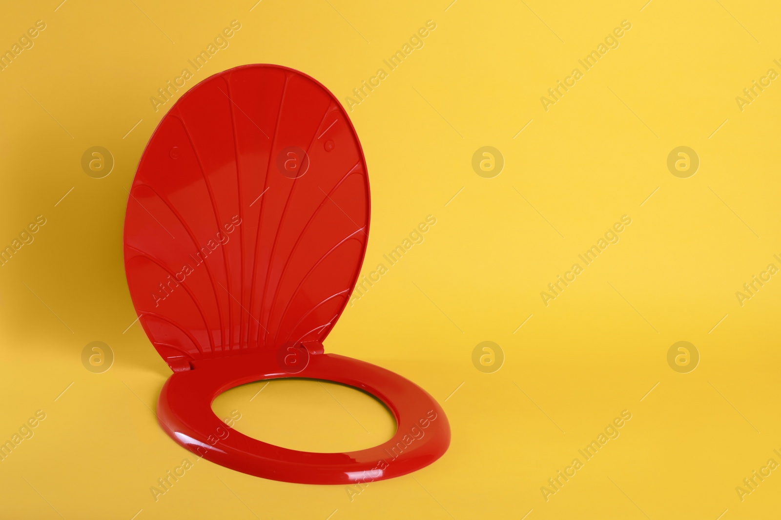 Photo of New red plastic toilet seat on yellow background, space for text