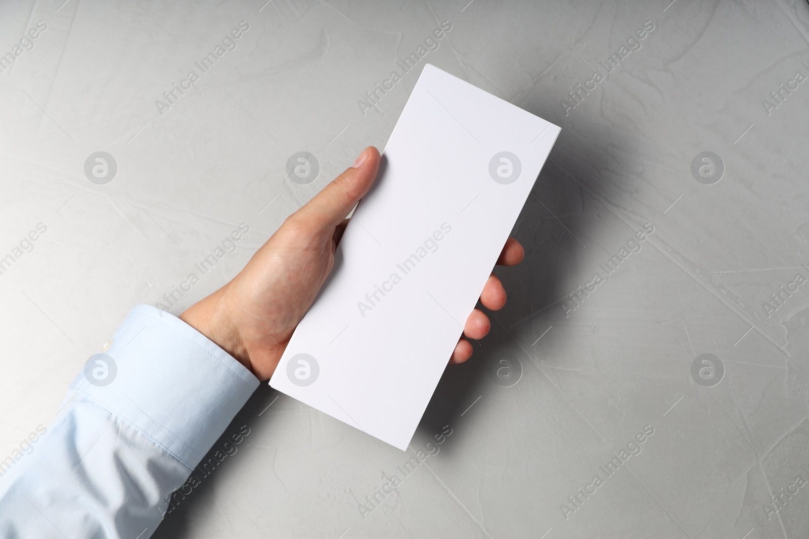 Photo of Man holding white blank card at light grey table, top view. Mockup for design