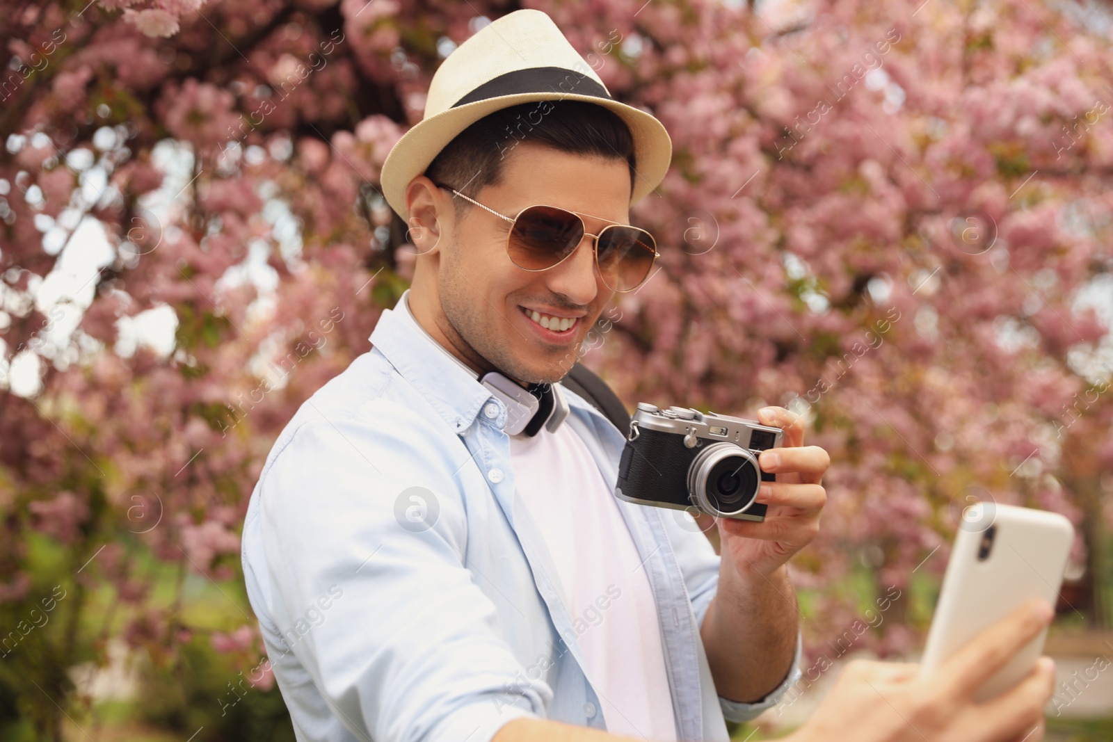 Photo of Happy male tourist taking selfie in blossoming park on spring day