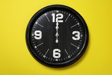 Photo of Modern black clock on yellow background, top view