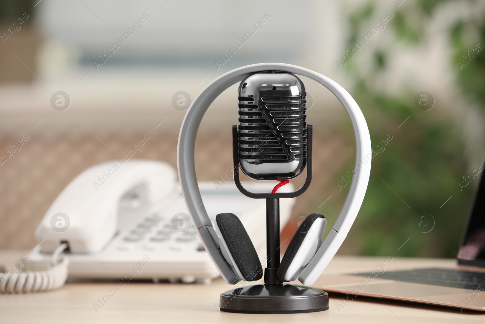 Photo of Microphone, modern headphones, laptop and desktop telephone on table indoors