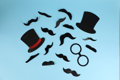 Photo of Fake mustaches, hats and glasses on light blue background, flat lay