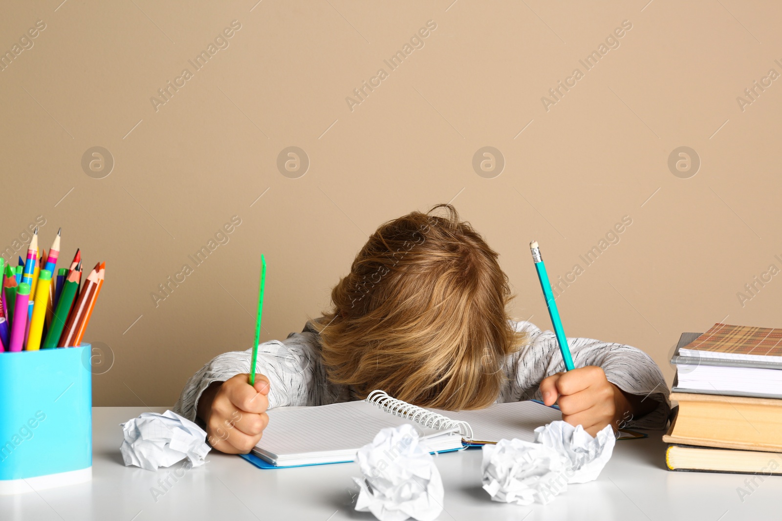 Photo of Tired little boy doing homework at table on beige background