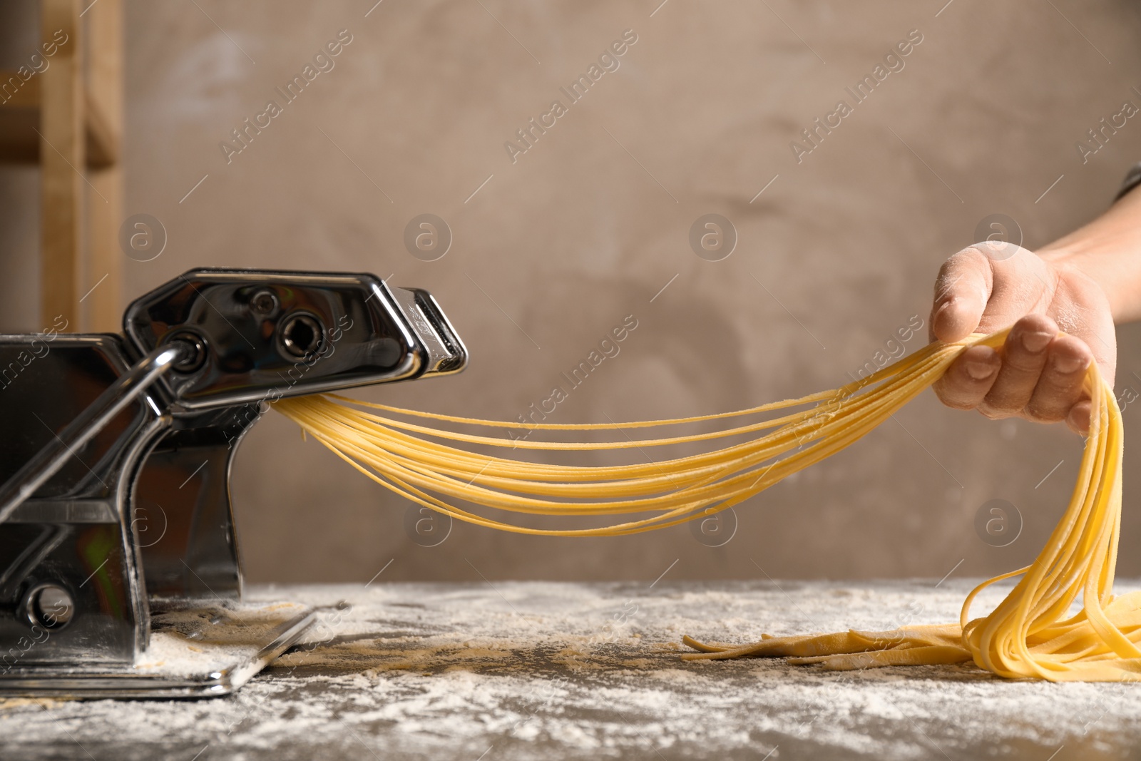 Photo of Woman preparing noodles with pasta maker machine at table, closeup