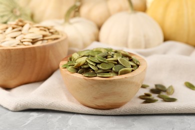 Wooden bowls with pumpkin seeds on grey marble table