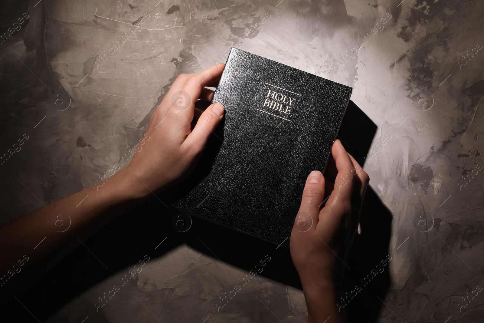 Photo of Religion. Christian woman praying over Bible at gray textured table, top view
