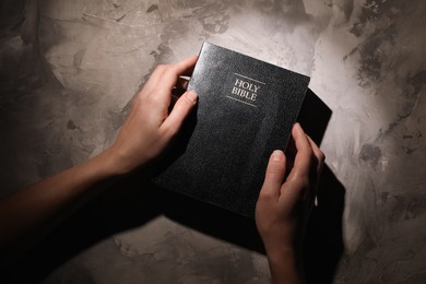 Religion. Christian woman praying over Bible at gray textured table, top view