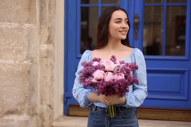 Photo of Beautiful woman with bouquet of spring flowers near building outdoors, space for text