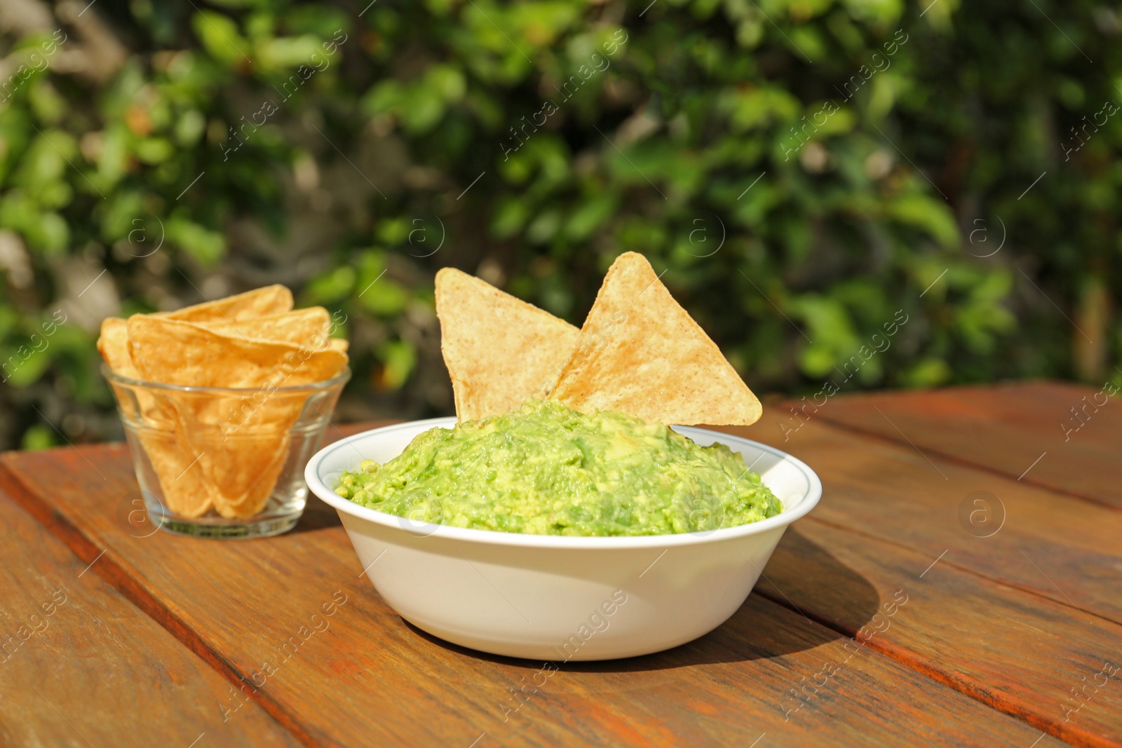 Photo of Delicious guacamole made of avocados with nachos on wooden table outdoors