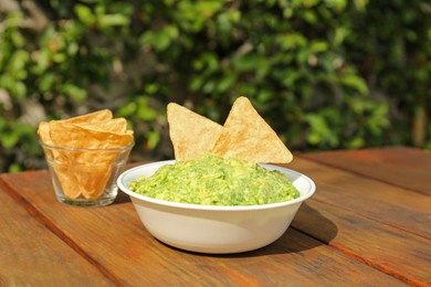 Delicious guacamole made of avocados with nachos on wooden table outdoors