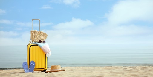 Yellow suitcase with beach items on sandy seashore, space for text