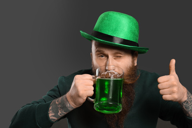 Photo of Bearded man drinking green beer on grey background. St. Patrick's Day celebration