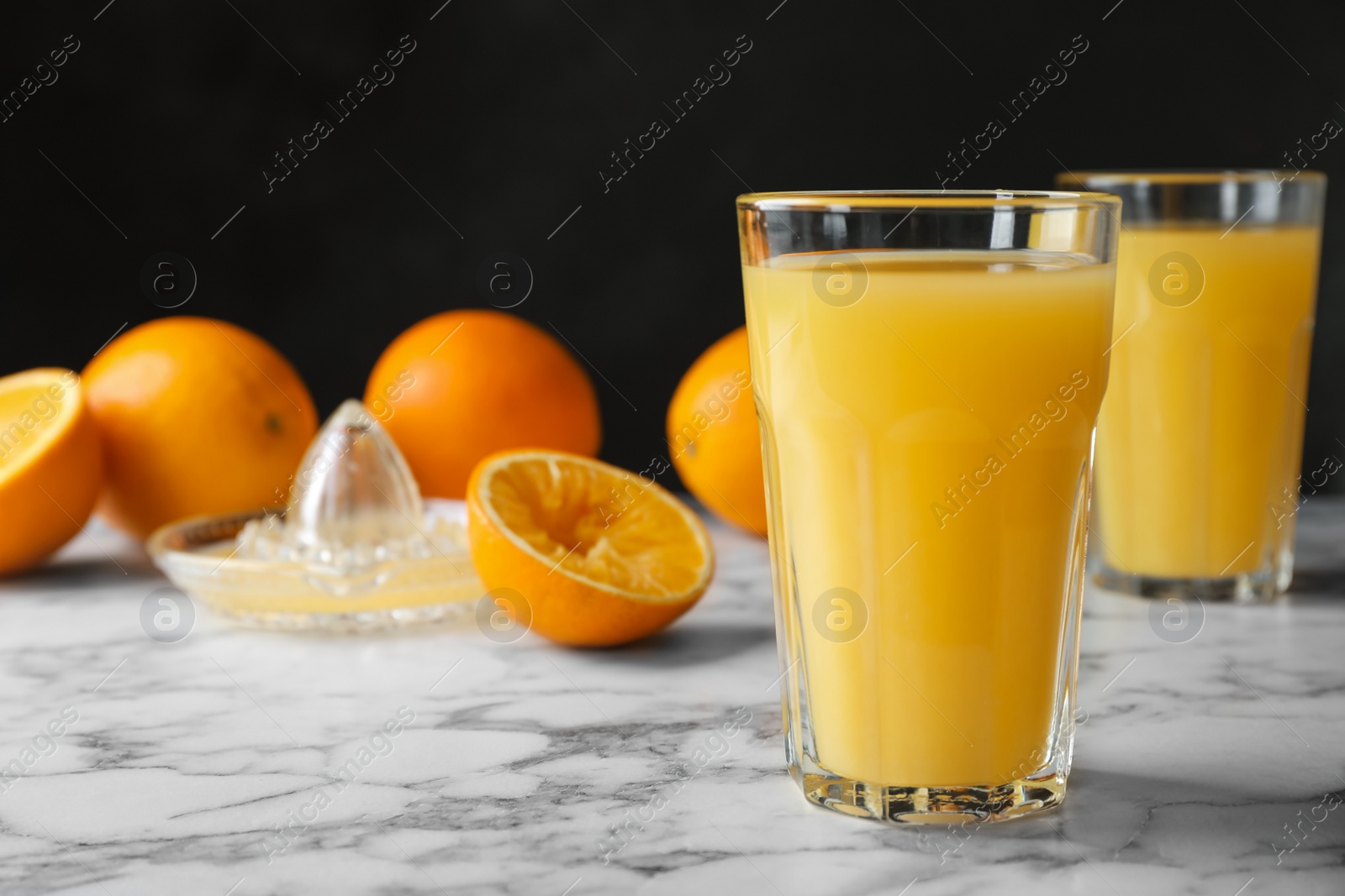 Photo of Glasses of orange juice on marble table. Space for text