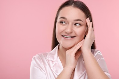 Smiling woman with dental braces on pink background. Space for text