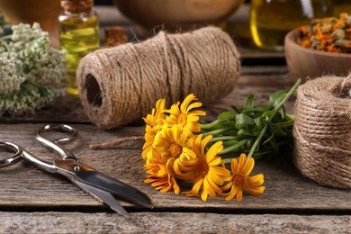 Photo of Calendula flowers, thread and scissors on wooden table, closeup. Medicinal herbs
