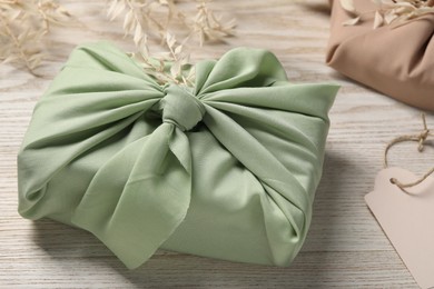 Photo of Furoshiki technique. Gift packed in light green fabric and dried branches on white wooden table, closeup