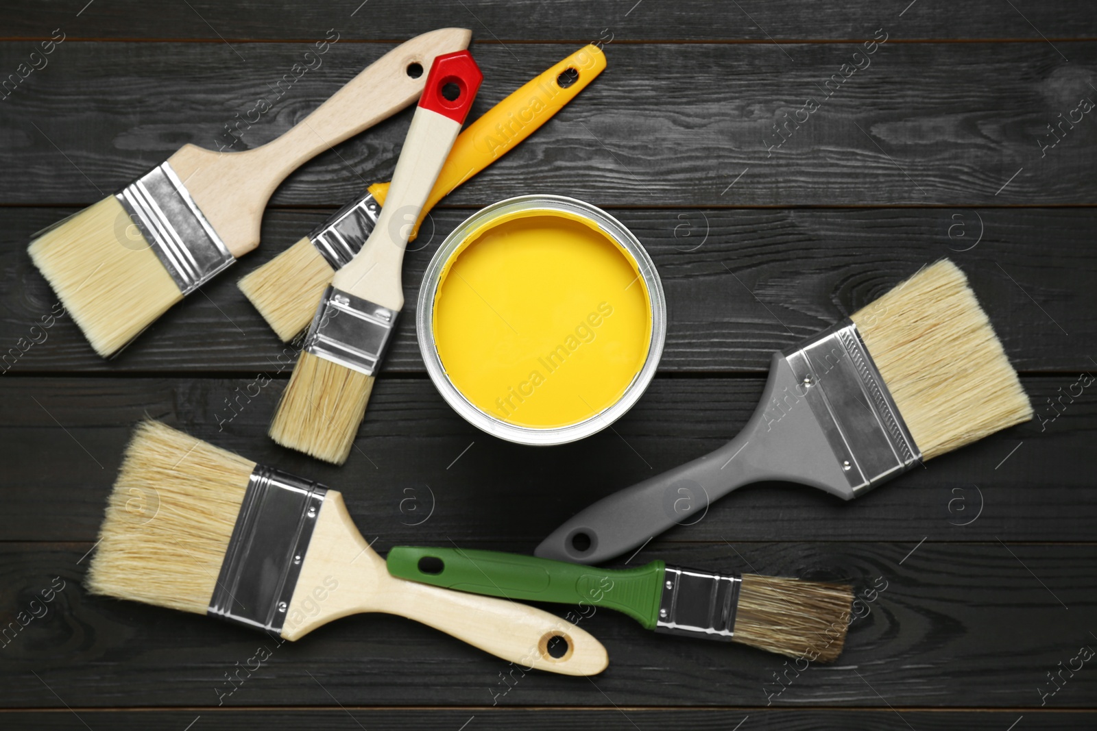 Photo of Can of yellow paint and brushes on black wooden table, flat lay