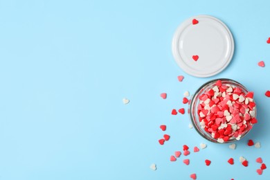 Photo of Bright heart shaped sprinkles and glass jar on light blue background, flat lay. Space for text