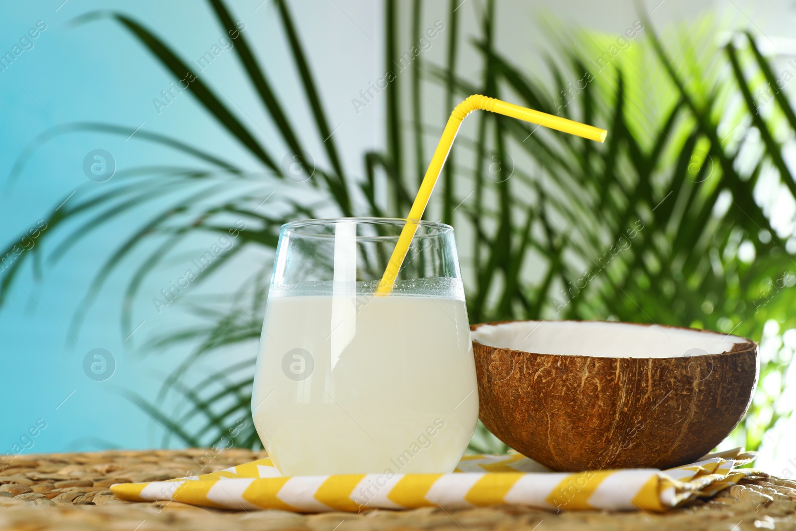 Photo of Composition with glass of coconut water on wicker table against blue background