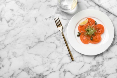 Photo of Salmon carpaccio with capers, microgreens and lemon served on white marble table, flat lay. Space for text