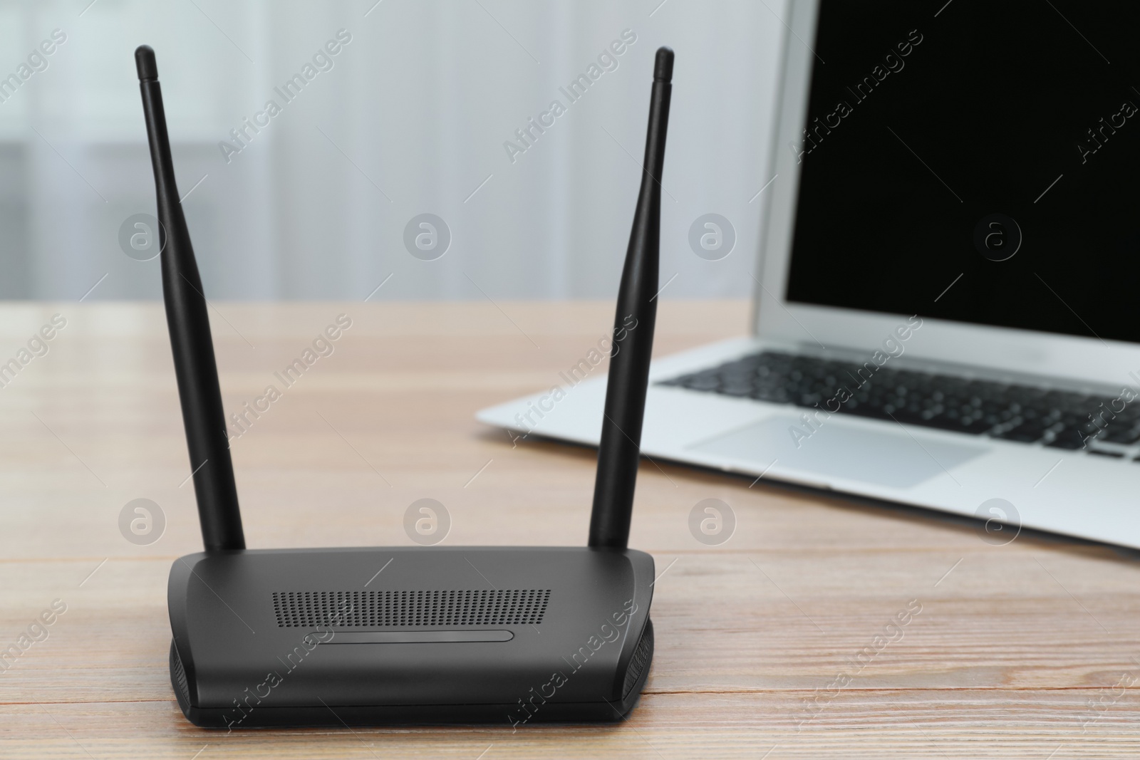 Photo of Modern Wi-Fi router and laptop on wooden table indoors