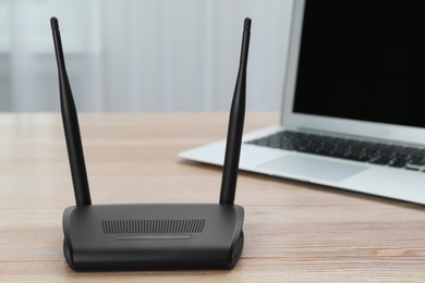 Photo of Modern Wi-Fi router and laptop on wooden table indoors