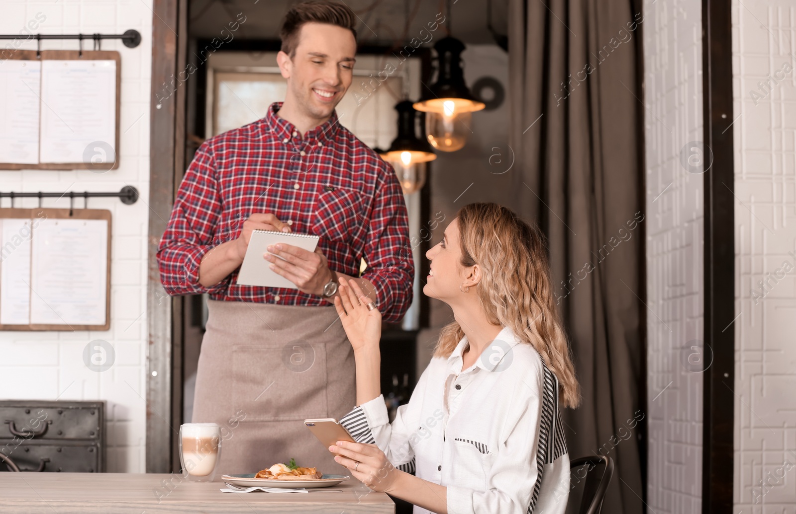 Photo of Young waiter taking order from client in restaurant