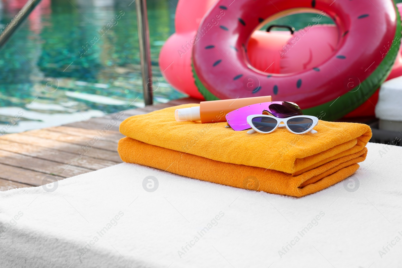 Photo of Beach towels, sunglasses and sunscreen on sunbed near outdoor swimming pool. Luxury resort