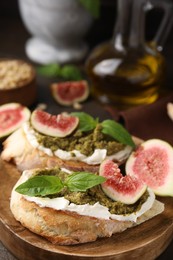 Photo of Tasty bruschettas with cream cheese, pesto sauce, figs and fresh basil on wooden board, closeup