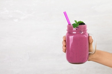 Young woman holding mason jar of tasty blackberry smoothie on light grey background, closeup. Space for text