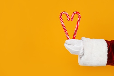 Photo of Santa Claus holding candy canes on yellow background, closeup of hand. Space for text
