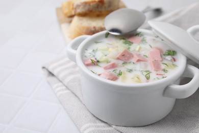 Photo of Delicious cold summer soup (okroshka) with boiled sausage in pot and spoon on white tiled table, closeup. Space for text