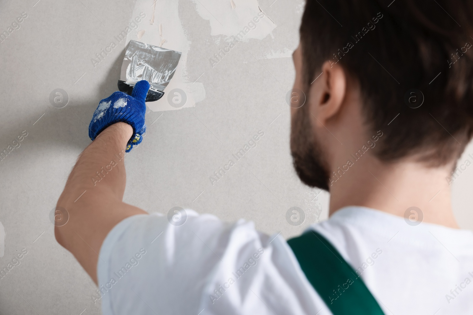 Photo of Worker in uniform plastering wall with putty knife indoors