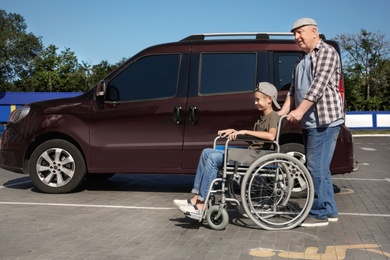 Photo of Senior man with boy in wheelchair near van on car parking