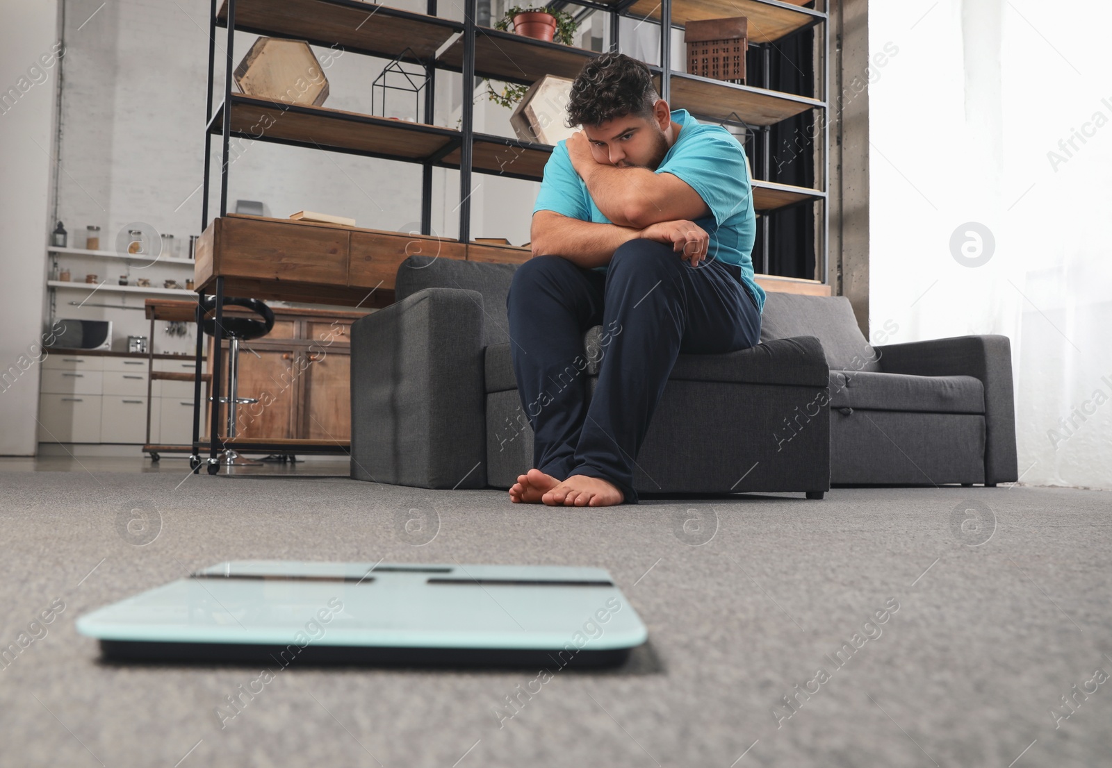 Photo of Depressed overweight man looking at scales in living room