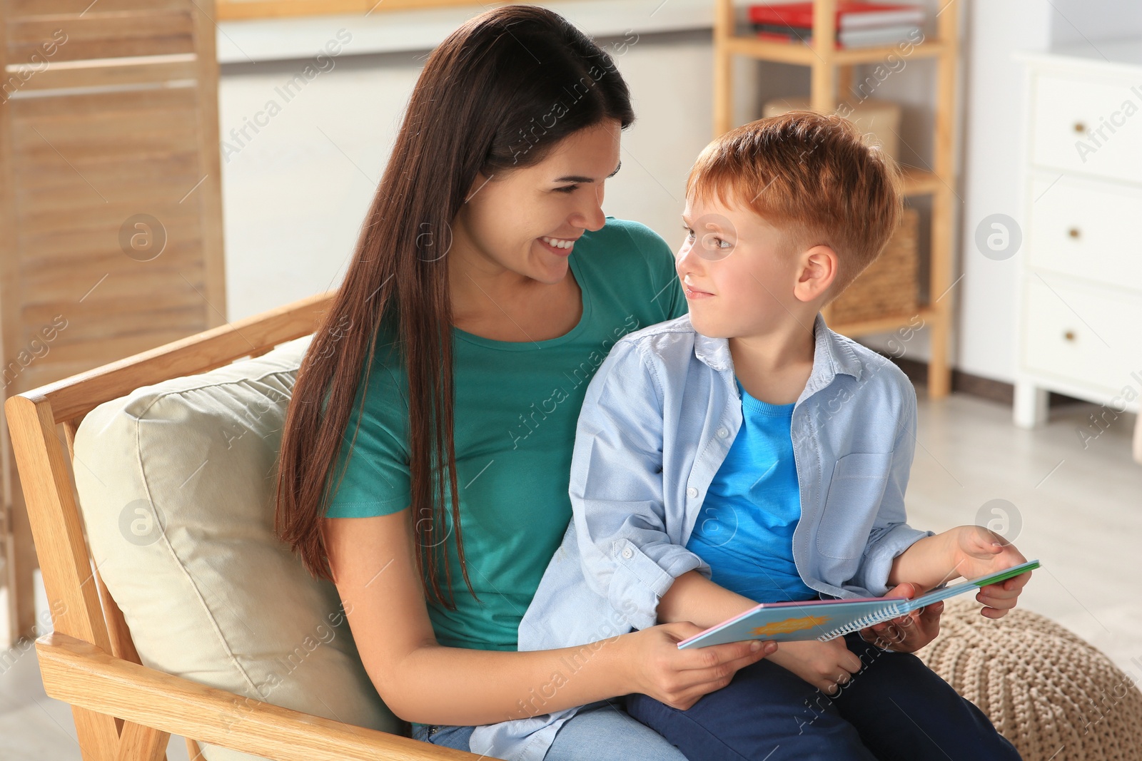 Photo of Mother reading book with her son on armchair in living room at home